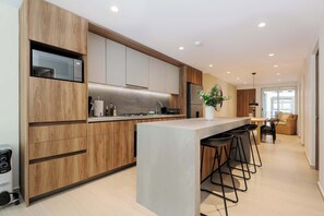Een moderne keuken met houten kastjes, een centraal eiland met barkrukken, en een zithoek met een bank en tafel.