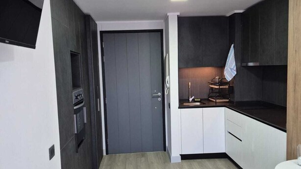 Ett modernt kök med mörka skåp, ett trägolv och en liten matplats.