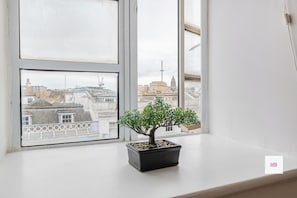 A potted plant on a windowsill with a view of buildings and a tower. - Brighton Central Gem, steps to beach and lanes (Brighton and Hove)