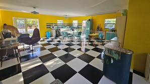 Ein Zimmer mit Schachbrettboden, gelben Wänden, einer Waschmaschine und einem Essbereich mit Stühlen und einem Tisch.