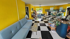 Ein Zimmer mit einem blauen Sofa, einem Schachbrettfußboden, einer Küchenzeile und Blick ins Freie.