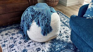 A living room with a brown sofa, a blue armchair, a white pouf, a large green plant, and a patterned rug. - Serene 3-bedroom townhome in charming Lompoc perfect for families (Lompoc)
