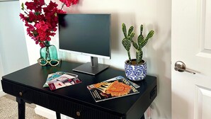 A black desk with a computer monitor, a vase with pink flowers, a potted cactus, and a magazine. - Serene 3-bedroom townhome in charming Lompoc perfect for families (Lompoc)