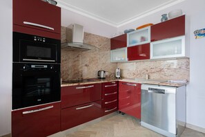 A kitchen with red cabinets, a black oven, a stainless steel dishwasher, and a marble countertop. - Central Juan les Pins – Spacious 3-Bedroom Sea View Apartment (Antibes)