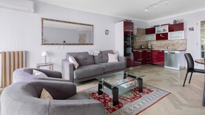 Ein modernes Wohnzimmer mit einer Couch, einem Glastisch und einer Küchenzeile mit roten Schränken und einem Geschirrspüler.