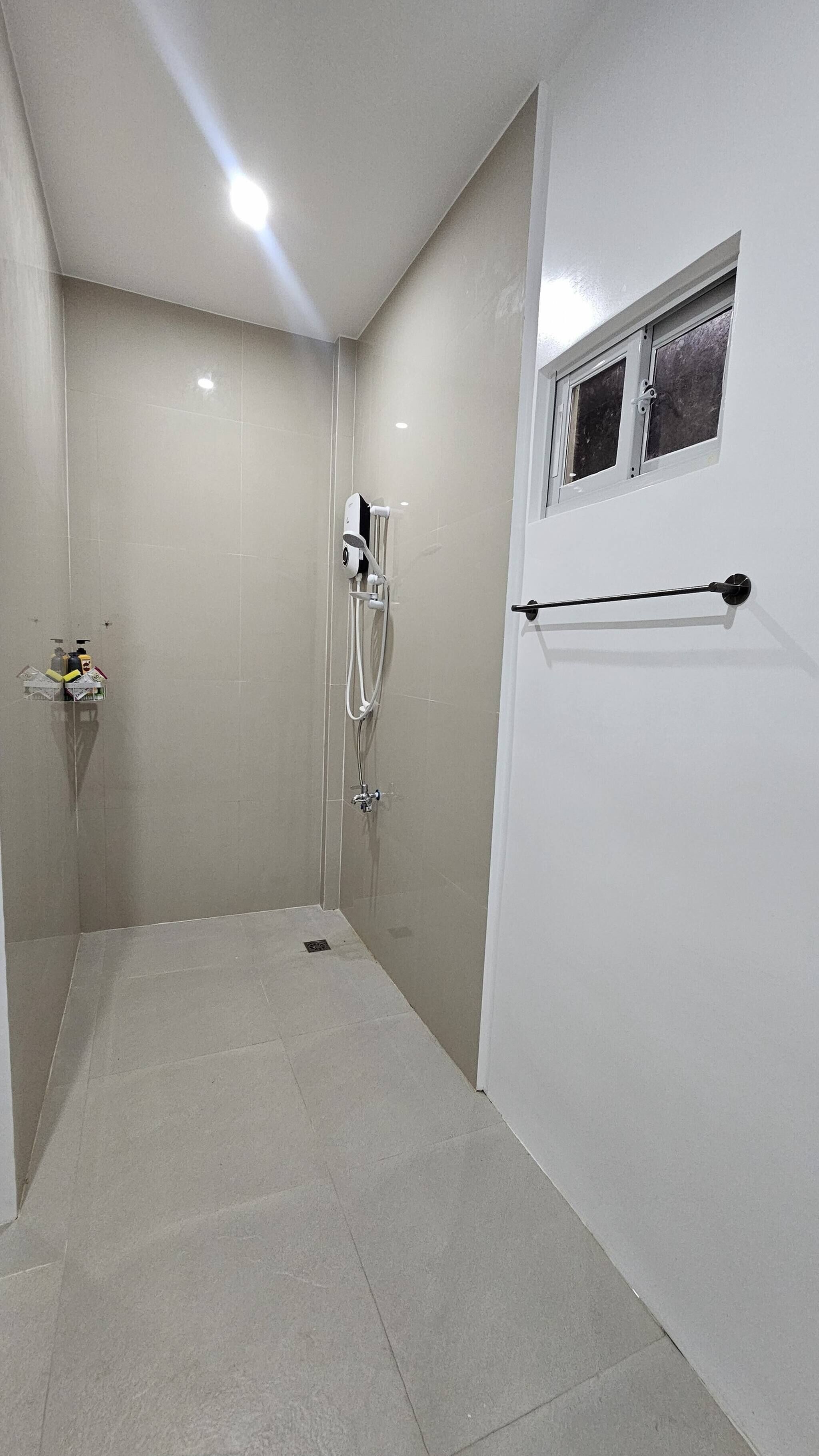 A small, tiled shower room with a window, a towel rack, and a showerhead.