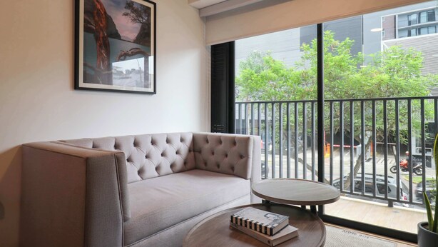 Ein modernes Wohnzimmer mit einer Couch, einem kleinen runden Tisch, einem gerahmten Bild an der Wand und einem Balkon mit Blick auf die Straße.