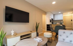 A modern living room with a flat-screen TV, a wooden console table, a round coffee table, a grey sofa, and a dining area with a glass table and chairs. - w* | Comfort Living 2BR w/ Balcony in San Isidro (San Isidro)