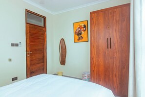 Une chambre à coucher avec un lit, une armoire en bois, un miroir fixé au mur et un tableau encadré.