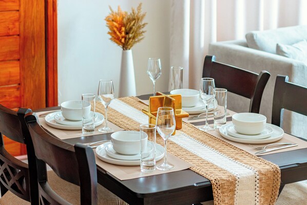 Une table à manger dressée avec des assiettes, des verres et un vase rempli de fleurs séchées.