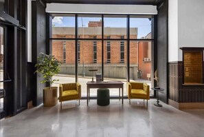 Una habitación amplia con ventanas grandes, una planta en maceta, dos sillones amarillos, una mesa redonda pequeña y una chimenea.