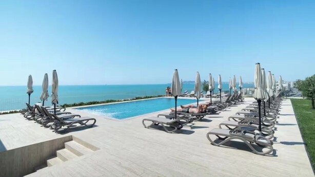 A poolside area with lounge chairs and umbrellas, a clear sky, and a view of the sea. - All Inclusive stay by PS - Durres Bay  (Rrashbull)