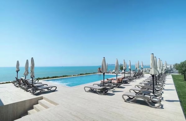 A poolside area with lounge chairs and umbrellas, a clear sky, and a view of the sea. - All Inclusive stay by PS - Durres Bay (Rrashbull)
