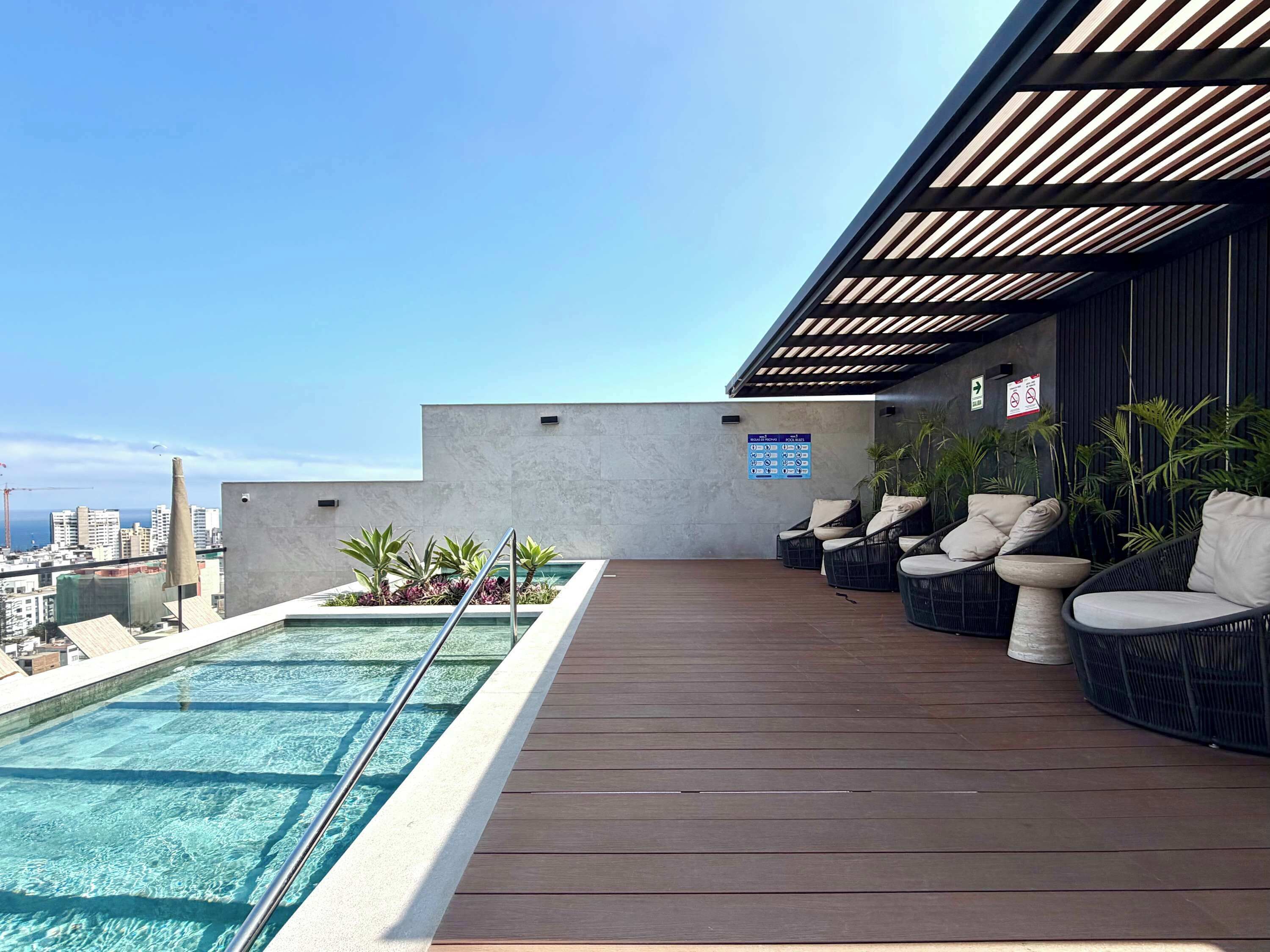 Un área de piscina en la azotea con vistas al horizonte de la ciudad, mobiliario exterior y cielo despejado.