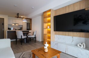 A modern living room with a wooden dining area, a flat-screen TV mounted on a wall, and a marble accent wall. - w* | Stunning 3BR w/ Balcony in Upscale Miraflores (Miraflores)