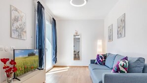 Un salon moderne avec un téléviseur à écran plat, un canapé agrémenté de coussins colorés et des œuvres d’art accrochées aux murs.