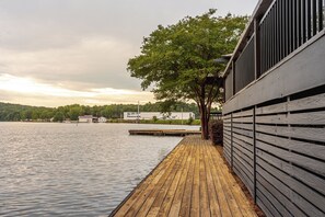 A wooden dock extending into a calm lake, a building with a sloped roof, and a tree in the background. - Creekside Lodge At Lake Martin (Dadeville)