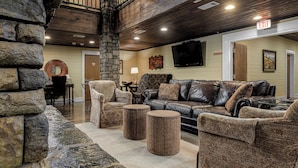 A cozy living room with a stone accent wall, leather sofas, and a flat-screen TV. - Creekside Lodge At Lake Martin (Dadeville)