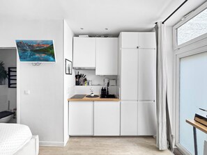 A compact kitchen with white cabinets, a wooden countertop, and a view of a mountain landscape through a window. - Studio, 18 m² • 3 min from the Champs-Élysées & the metro (Paris)