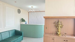 A reception area with a green sofa, a marble wall, a clock, and a decorative statue.