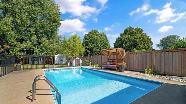 A rectangular swimming pool with a metal ladder, surrounded by a wooden fence, a wooden deck, and a covered seating area. - Tranquil poolside retreat!  Basement with 2 rooms! Close to Niagara Falls. (Niagara Falls)