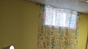 A room with a table, a chair, a lamp, a window with floral curtains, and a towel rack. - Tranquil poolside retreat!  Basement with 2 rooms! Close to Niagara Falls. (Niagara Falls)