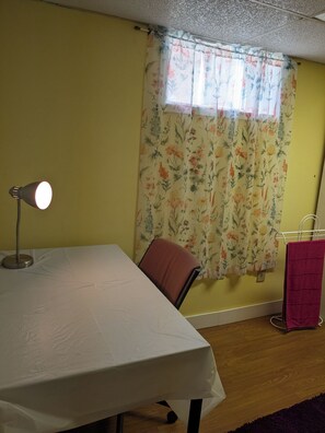Habitació amb taula, cadira, làmpada, finestra amb cortines florals i un suport per tovalloles.