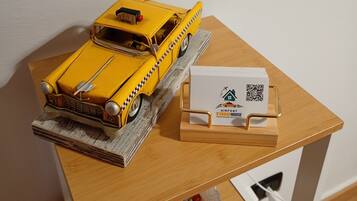 Ein gelbes Modelltaxi auf einer Holztischplatte, eine weiße Schachtel mit einem QR-Code und eine Schale mit bunten Bonbons.