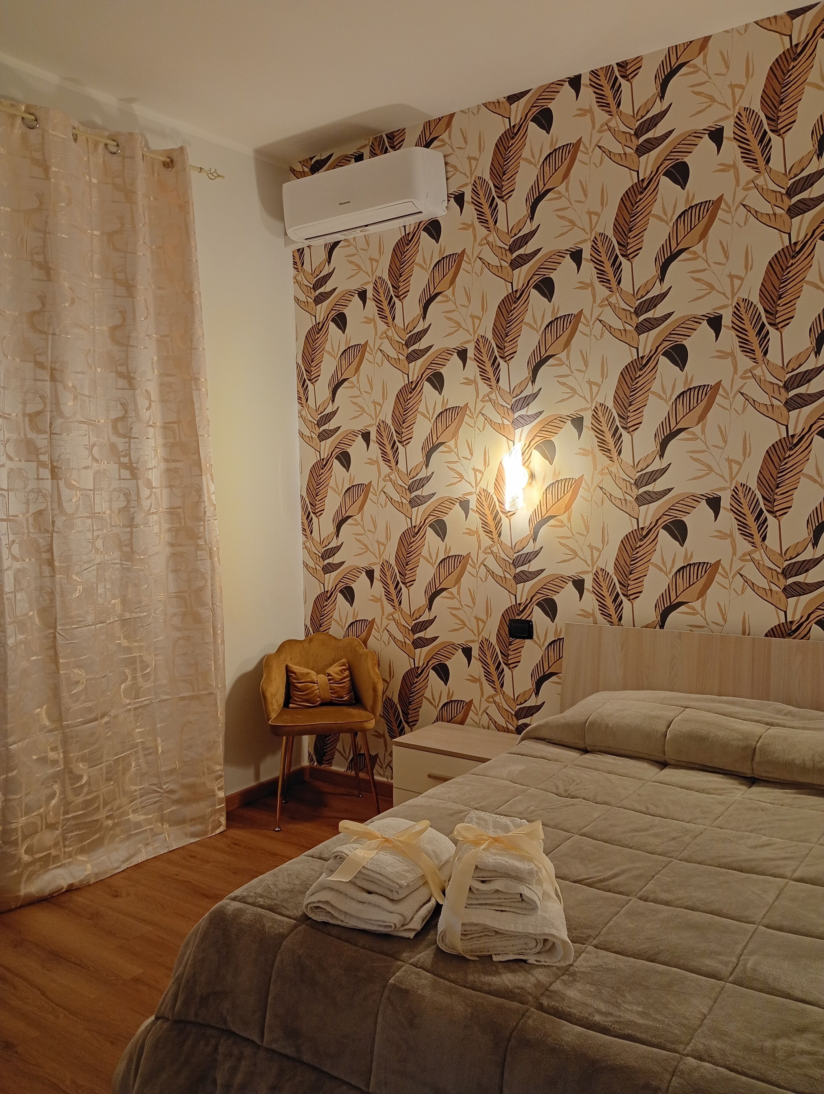 Ein Schlafzimmer mit einem Bett, einem Sessel, einer Klimaanlage und einer Wand mit einem Blattmuster.