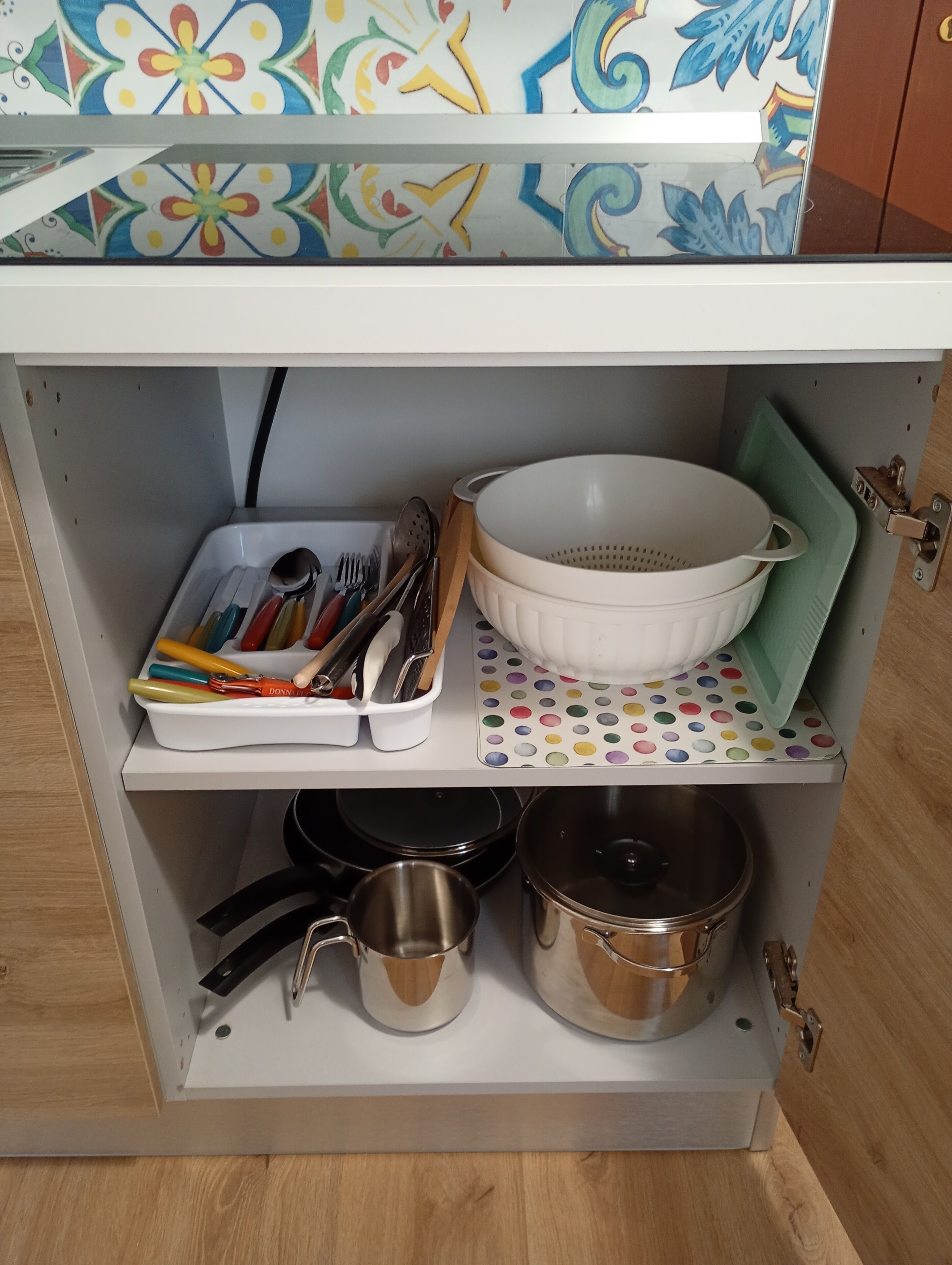 Une étagère de cuisine avec des ustensiles, une passoire, des casseroles et un pare-éclaboussures à motifs.