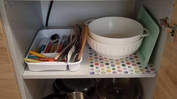 Une étagère de cuisine avec des ustensiles, une passoire, des casseroles et un pare-éclaboussures à motifs.