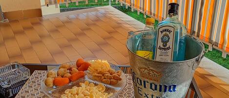 A balcony with a table set for a meal, a bottle of Bombay Sapphire gin, and two glasses of a dark beverage.