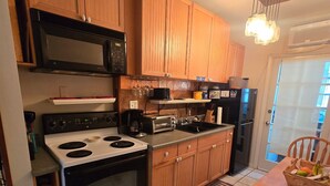 Una cocina con armarios de madera, estufa, microondas y un comedor con una silla y mesa.