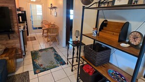 Una sala de estar con televisor, una mesa de centro de madera, un tapete, una estantería y una puerta que da a otra habitación.