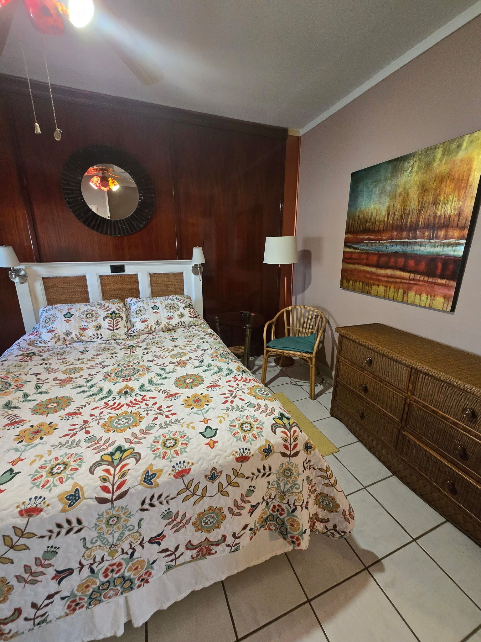 Un dormitorio con una cama grande, una silla, un tocador, un espejo y un cuadro en la pared.