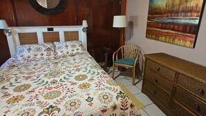 Un dormitorio con una cama grande, una silla, un tocador, un espejo y un cuadro en la pared.