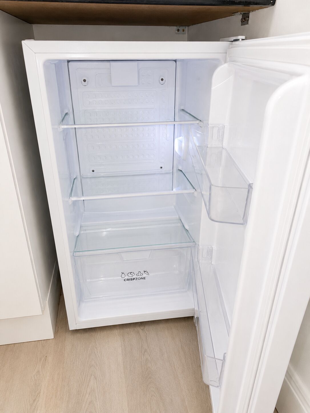 An open refrigerator with clear plastic shelves and a label 'CRISPZONE' on the bottom shelf.