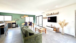 A modern living room with a sofa, coffee table, and TV. There's a dining area with chairs and a table. - Villa Les Vignes – 8 guests in the Gard (Saint-Chaptes)