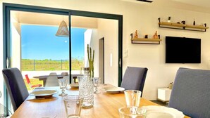 A dining table set with plates, glasses, and cutlery, with a view of a vineyard through a glass door. - Villa Les Vignes – 8 guests in the Gard (Saint-Chaptes)