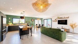 A modern kitchen with a dining area, a green sofa, and a TV mounted on the wall. - Villa Les Vignes – 8 guests in the Gard (Saint-Chaptes)