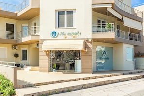 A multi-story building with balconies, a storefront with a sign, and a visible entrance. - 3 Bedroom Spacious  Modern Apartment with Patio (Iraklio)