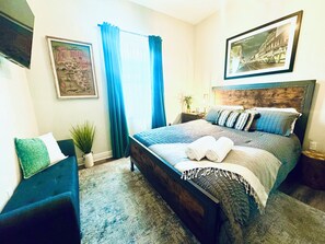 A bedroom with a bed, a chair, a nightstand, a lamp, a framed picture, and a window with curtains. - Charming 3-bedroom house in Ybor/Tampa! Walk to Trolley for events (Tampa)