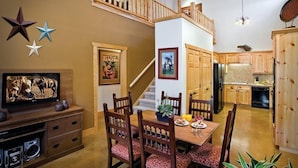 A dining area with a wooden table and chairs, a staircase, and a kitchen with wooden cabinets. - New Braunfels | Friends River Escape | Pool + River | 2BR (New Braunfels)
