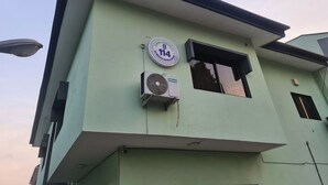A building with a green facade, a circular sign with the number 114, and an air conditioning unit mounted on the wall. - 114 Luxury Apartments by Oragon Hotel (Lagos)