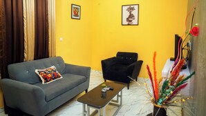 A living room with a grey sofa, a black armchair, a small coffee table, and two framed artworks on the wall. - 114 Luxury Apartments by Oragon Hotel (Lagos)