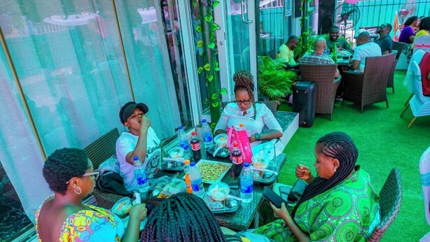 An outdoor dining area with wicker furniture, glass partitions, and potted plants. - 114 Luxury Apartments by Oragon Hotel (Lagos)