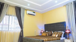 A bedroom with a large bed, an air conditioning unit, a bedside lamp, and curtains. - 114 Luxury Apartments by Oragon Hotel (Lagos)