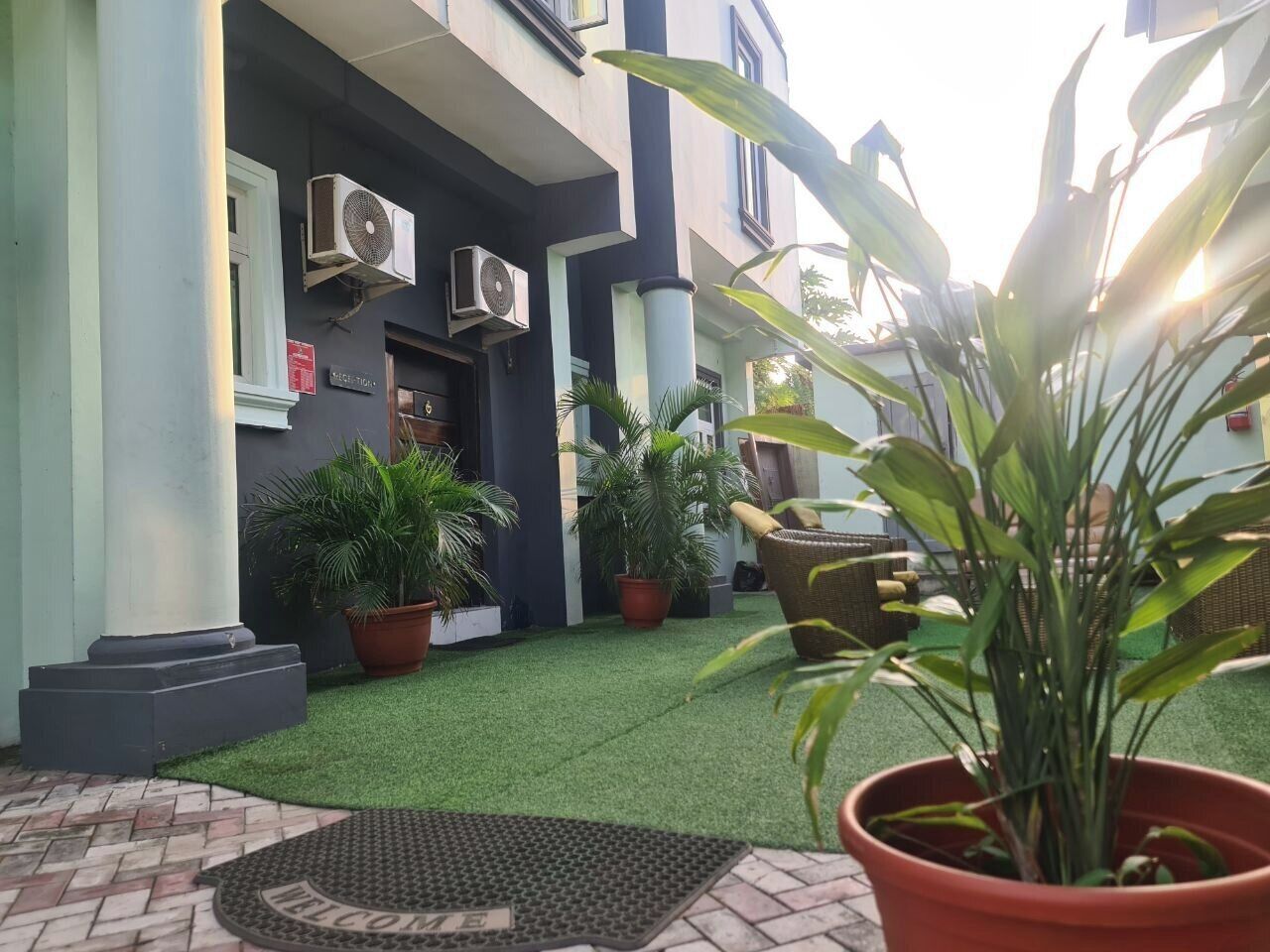 A building with a dark facade, air conditioning units, potted plants, and a welcome mat.