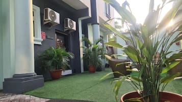 A building with a dark facade, air conditioning units, potted plants, and a welcome mat.