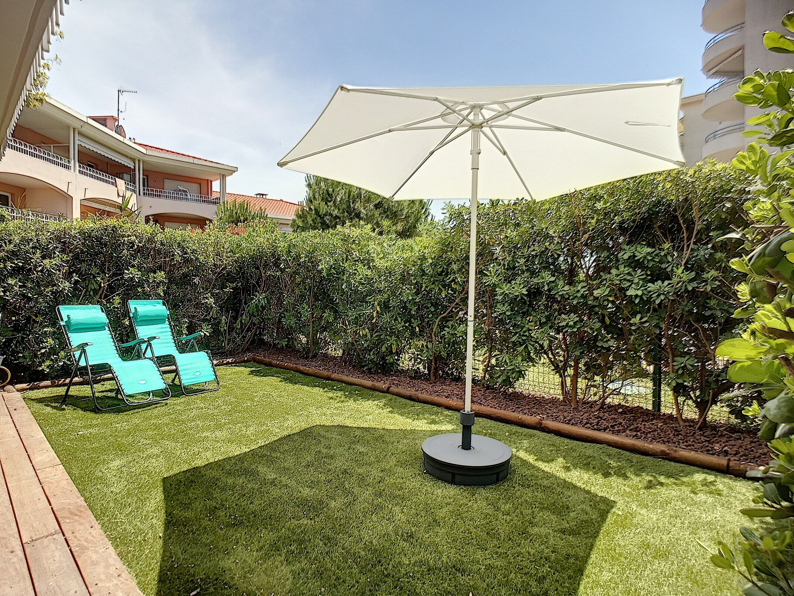 A well-maintained outdoor area with artificial grass, a large umbrella, and two lounge chairs.